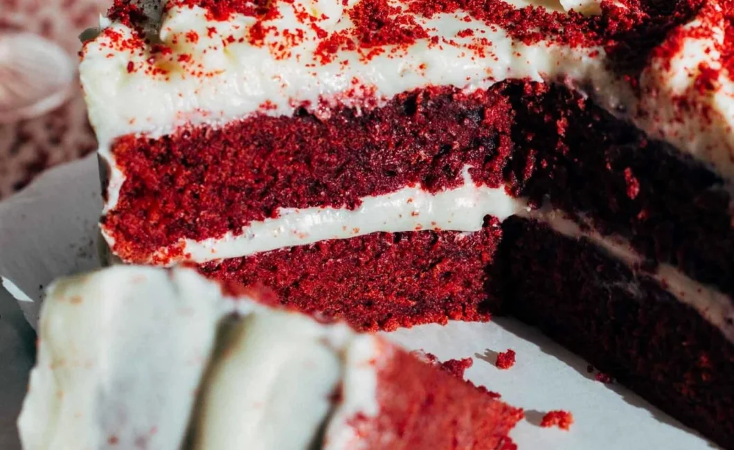 Photo of double layer red velvet cake with white icing. One slice lies on it's side in front of the cake.