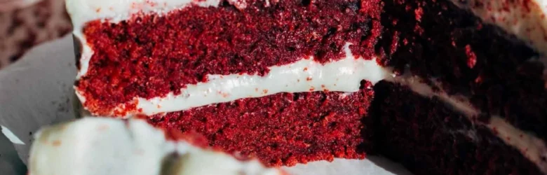 Photo of double layer red velvet cake with white icing. One slice lies on it's side in front of the cake.